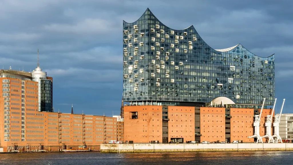 Symfoniczna orkiestra występująca na tle nowoczesnej architektury portowego miasta.